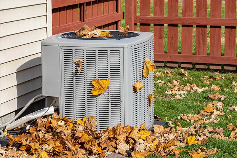 Residential outdoor condenser surrounded by leaves and due for AC replacement