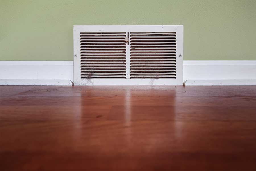 Older wall vent with accumulated dust connected to residential HVAC ductwork